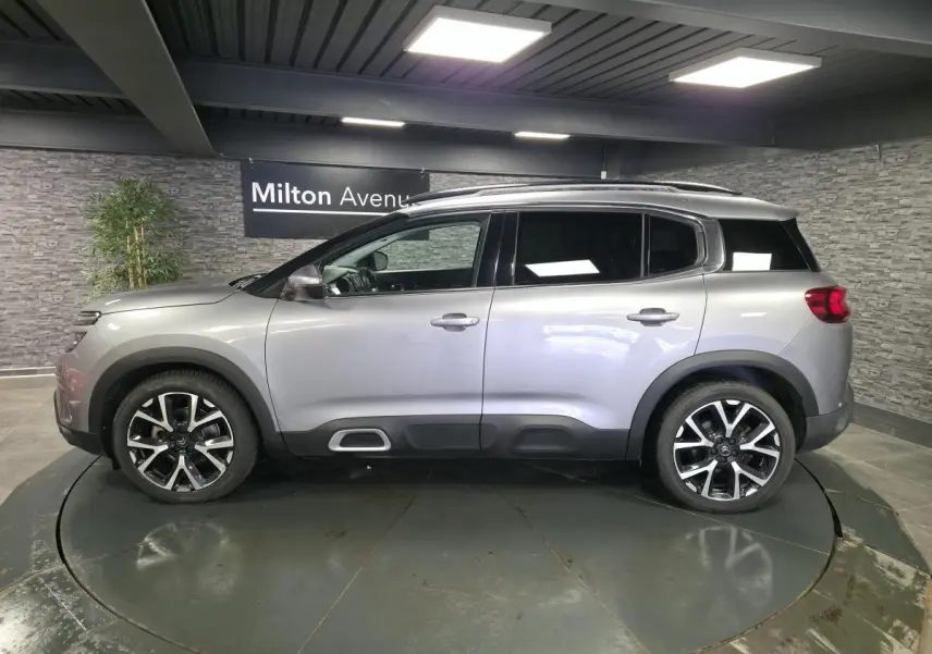 Profil droit d'un Citroën C5 Aircross gris métallisé avec jantes alliage 19 pouces et barres de toit bi-ton.