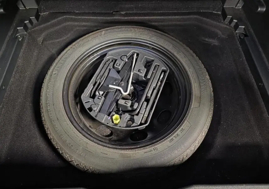 Gros plan sur la roue de secours galette noire et son kit de réparation dans le coffre d'un Citroën C5 Aircross gris.