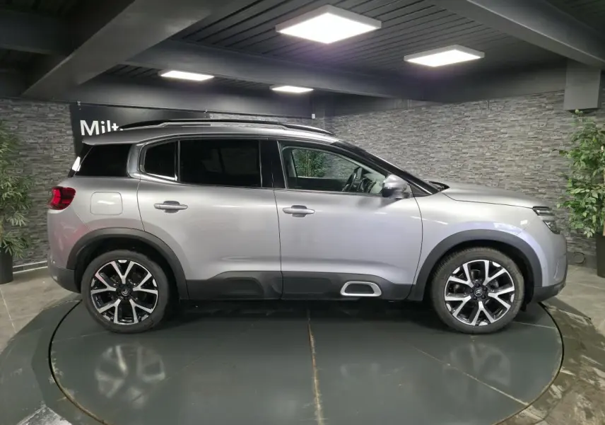 Vue de profil côté gauche d'un Citroën C5 Aircross gris métallisé avec jantes alliage 19 pouces dans un showroom.