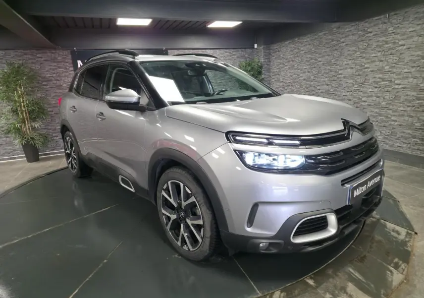 Vue 3/4 avant droit d'un Citroën C5 Aircross gris métallisé avec jantes alliage 19 pouces et barres de toit noires.