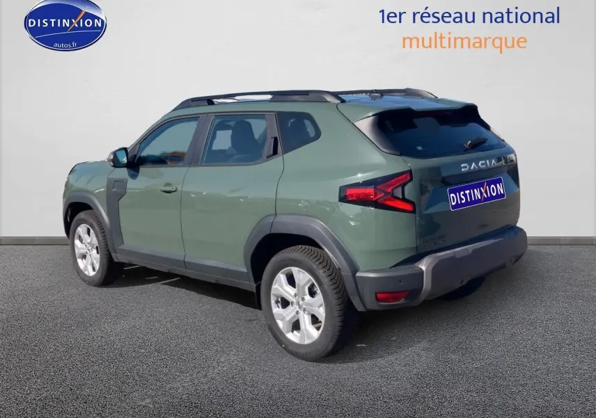 Vue 3/4 arrière droite d'un Dacia Duster 2026 kaki lichen avec barres de toit et jantes alu visibles.