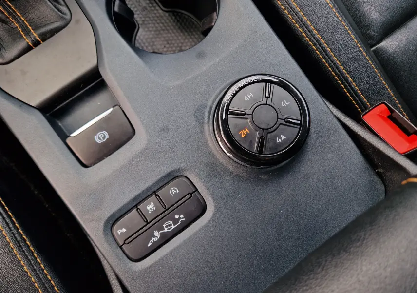 Gros plan sur la console centrale noire du Ford Ranger Wildtrak 2023, avec molette de modes de conduite et coutures orange.
