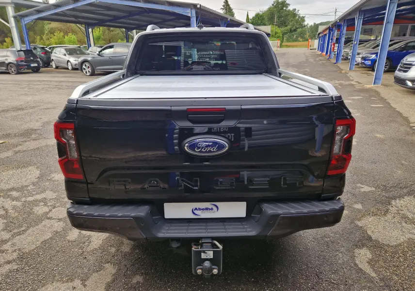Vue arrière d'un Ford Ranger Wildtrak noir 2023 avec rideau de plateau coulissant et attelage visible.