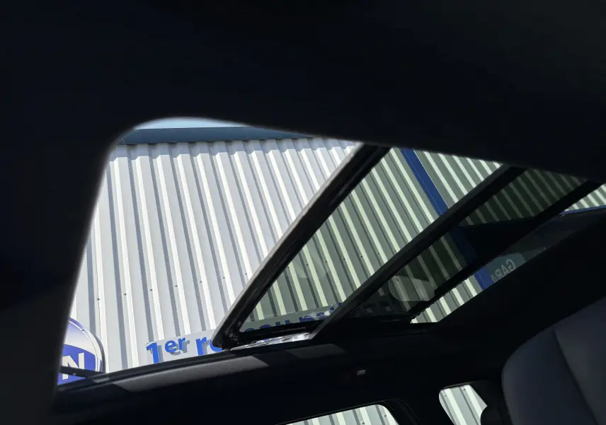 Toit panoramique ouvert vu de l'intérieur d'un JAECOO J7 noir crystal, avec ciel et bâtiment en arrière-plan.