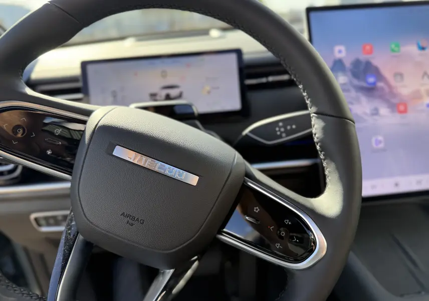 Gros plan sur le volant noir du JAECOO J7 PHEV 2026, avec tableau de bord numérique et écran tactile en arrière-plan.