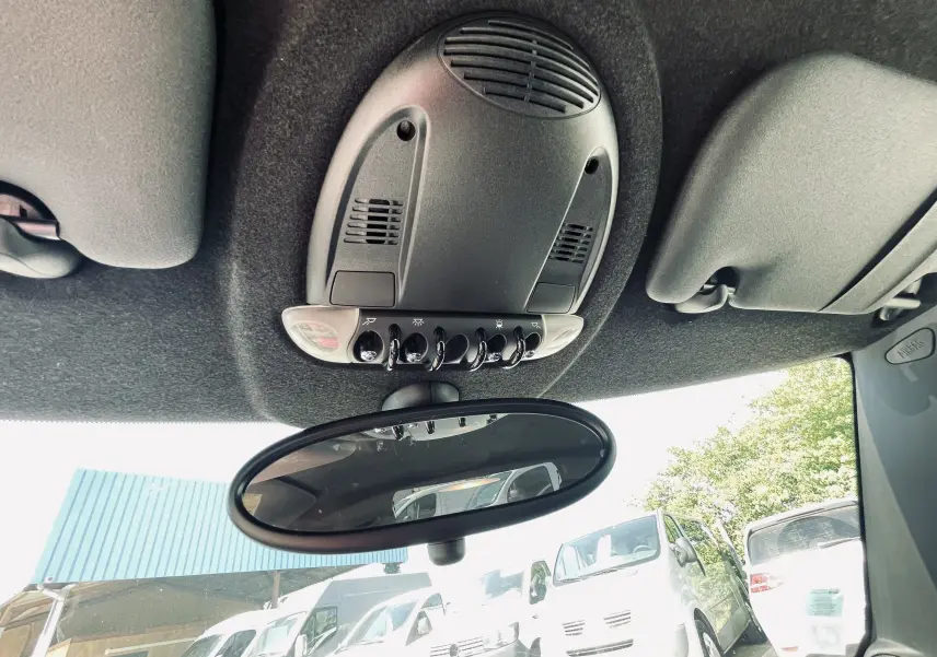 Plafonnier et rétroviseur intérieur de la MINI Cooper S gris, vue de l'habitacle vers l'avant avec parkings visibles dehors.