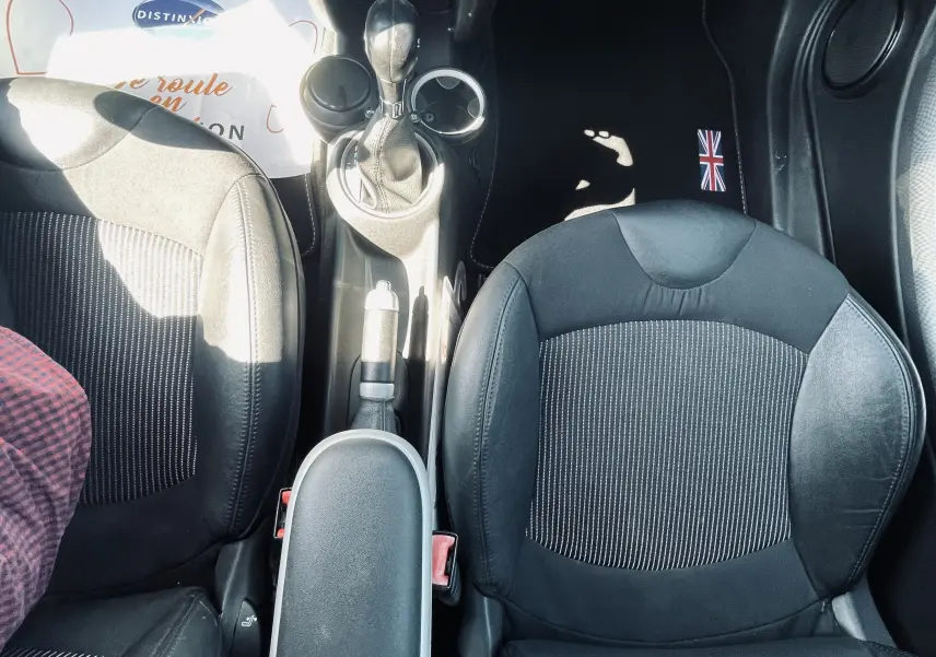 Vue plongeante sur l'intérieur avant noir d'une MINI Cooper S 2008 avec console centrale et sièges en tissu rayé.