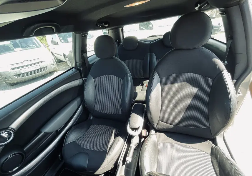 Vue intérieure avant de la MINI Cooper S 2008 montrant les sièges avant en tissu noir et cuir avec appuie-têtes ronds.