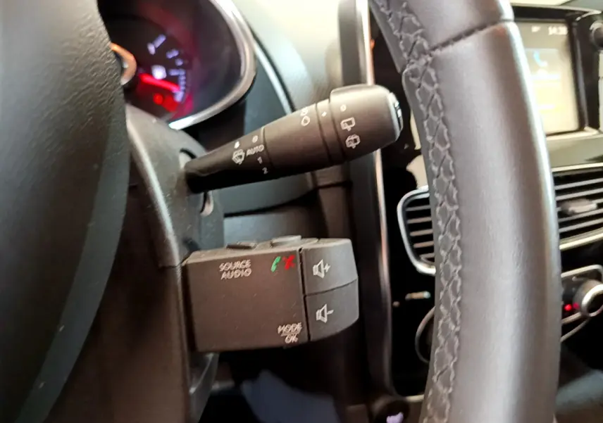 Gros plan sur la commande audio au volant cuir noir d'une Renault Clio Business blanche, tableau de bord et écran tactile en arrière-plan.