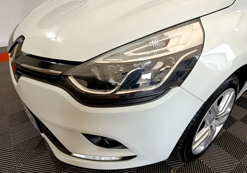 Gros plan sur l'avant droit d'une Renault Clio Business TCe 90 blanche, mettant en valeur son phare et la calandre noire brillante.