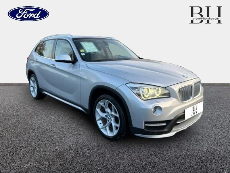 BMW X1 xDrive25dA Mineralgrau vue 3/4 avant droit avec phares allumés et jantes alu distinctives