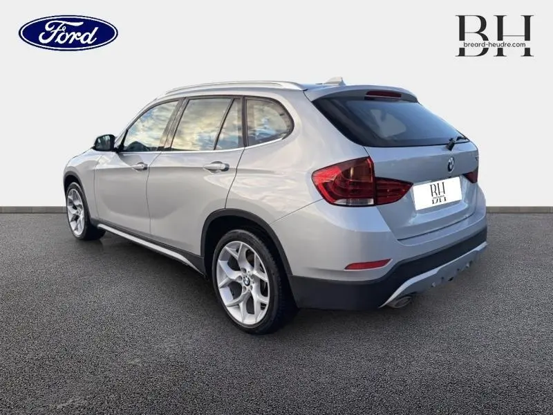 BMW X1 xDrive25dA Mineralgrau vue 3/4 arrière droit, soulignant ses jantes alu et barres de toit chromées.