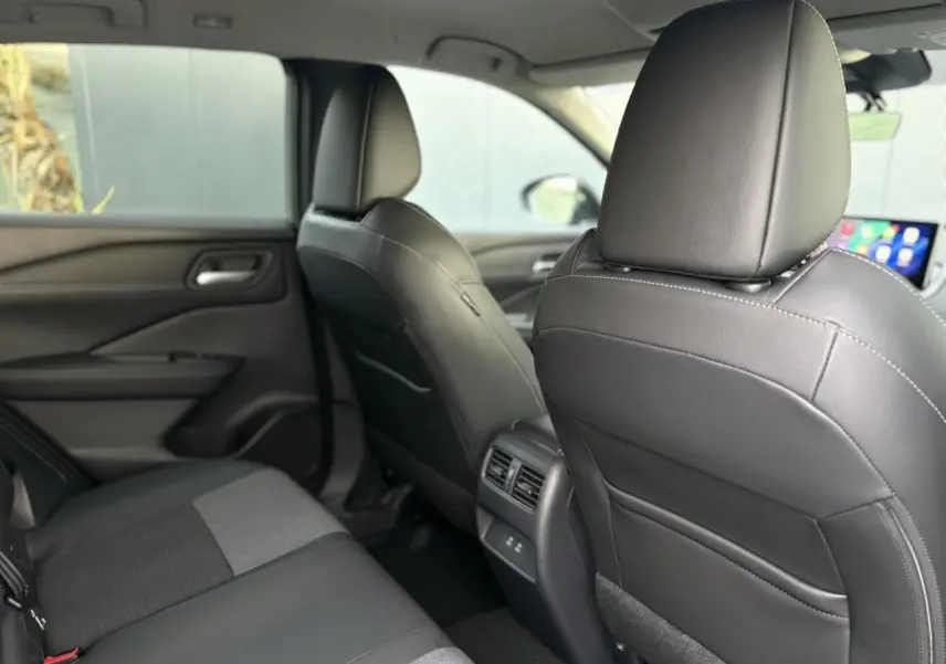 Vue intérieure arrière du Nissan Qashqai 2025, sièges noirs en cuir et tissu avec console centrale et ports USB visibles.