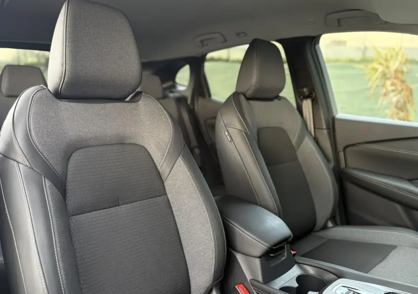 Vue intérieure des sièges avant gris foncé et tissu noir du Nissan Qashqai III e-Power, avec accoudoir central et porte-gobelets.