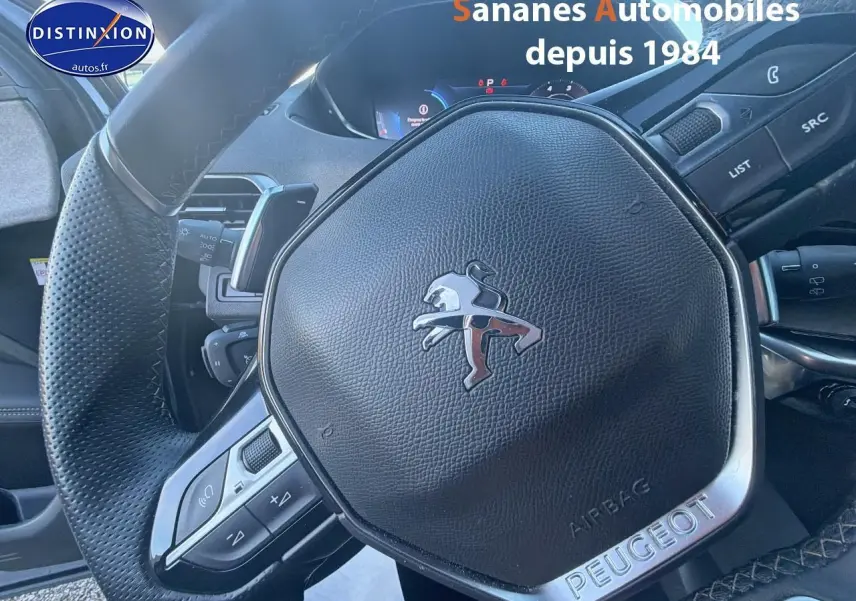 Gros plan sur le volant cuir perforé Peugeot du 3008 2023, avec commandes intégrées et badge chromé GT.