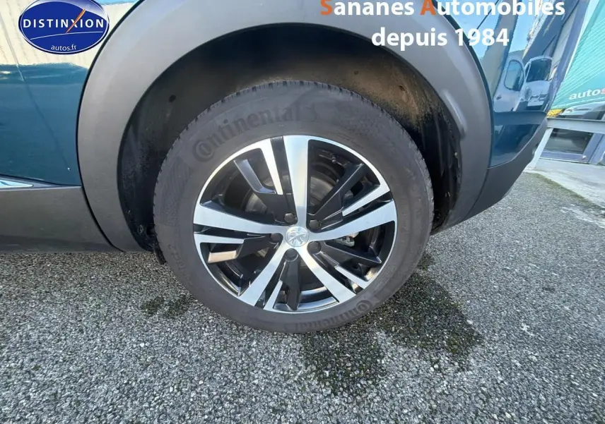 Gros plan sur la roue avant droite du Peugeot 3008 bleu avec jante alliage bicolore et logo Peugeot central.