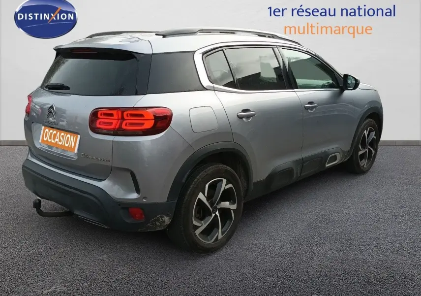 Vue 3/4 arrière droite d'un Citroën C5 Aircross gris Artense métallisé avec feux arrière allumés et attelage visible.