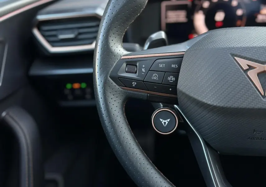 Gros plan sur le volant perforé noir avec logo CUPRA cuivré et commandes multifonctions de la Leon 2025.