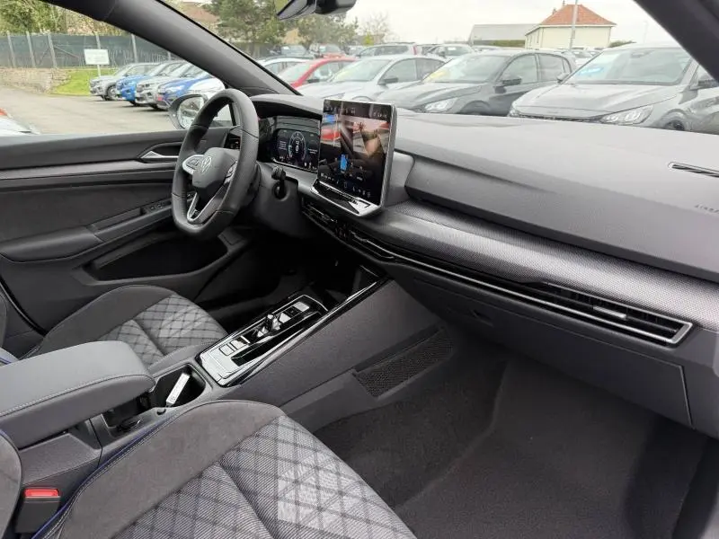 Vue intérieure côté conducteur de la Volkswagen Golf 2.0 TDI R-Line 2026 avec écran tactile et sièges tissu gris à motifs.