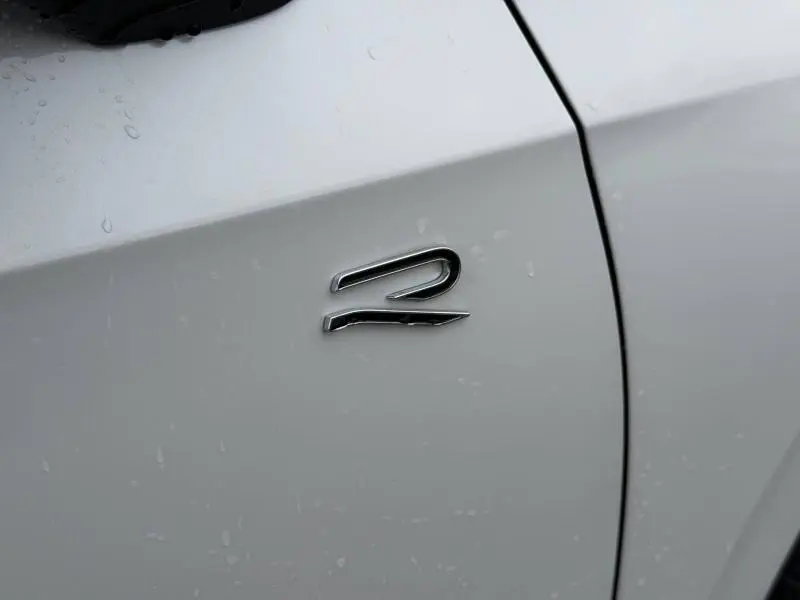 Gros plan sur l'emblème "R" chromé sur la porte blanche oryx nacrée d'une Volkswagen Golf 2.0 TDI 150ch R-Line 2026.