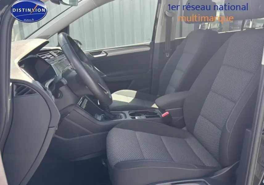 Vue intérieure côté conducteur du Volkswagen Touran 2025 noir, sièges tissu gris et volant cuir multifonction.