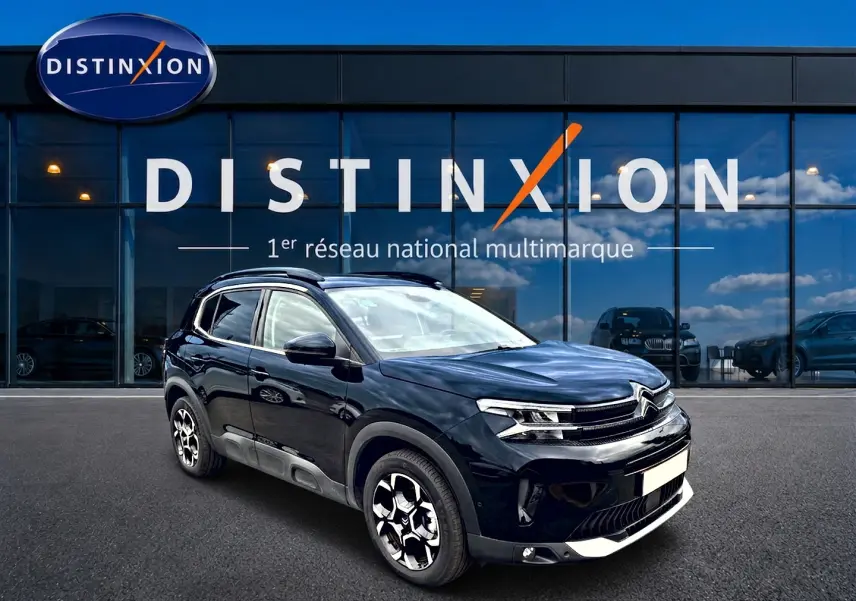 Citroën C5 Aircross noir en 3/4 avant droit, avec jantes alu et barres de toit visibles devant une vitrine Distinxion.