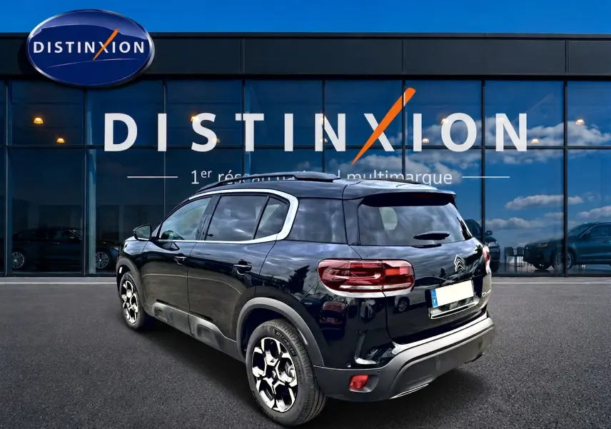 Vue 3/4 arrière droite du Citroën C5 Aircross noir 2025 avec jantes alu et barres de toit visibles.