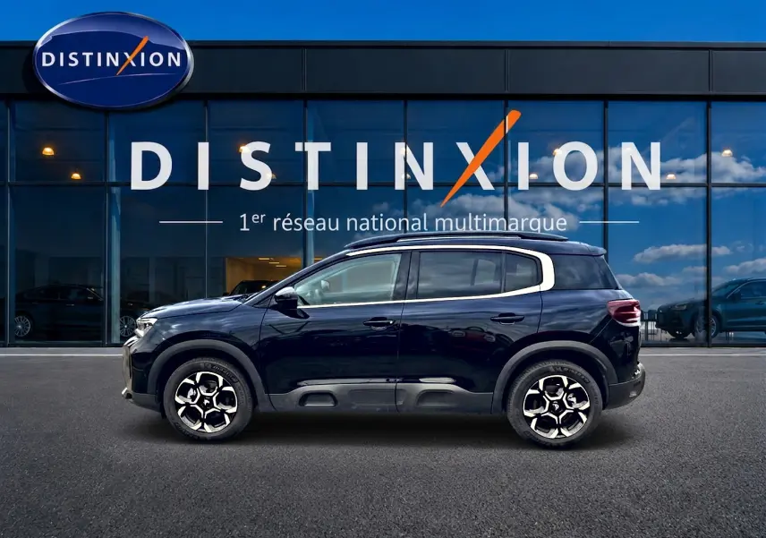 Profil côté gauche d'un Citroën C5 Aircross noir 2025 devant une vitrine avec logo Distinxion.