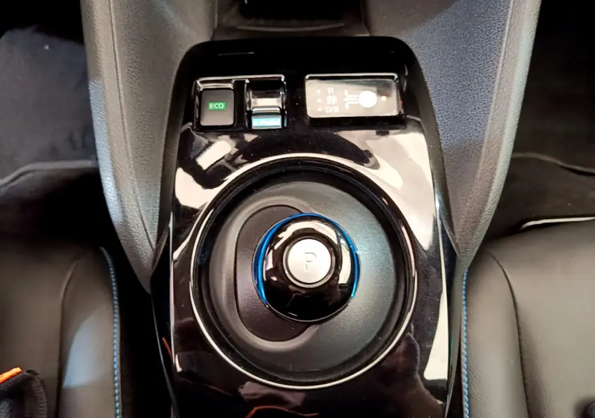 Gros plan sur la commande de boîte automatique noire avec bouton de stationnement bleu dans l'habitacle du Nissan Leaf blanc.