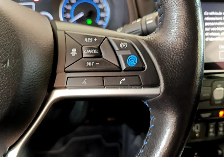 Gros plan sur le côté gauche du volant cuir noir de la Nissan Leaf blanche, avec commandes de régulateur et assistance.