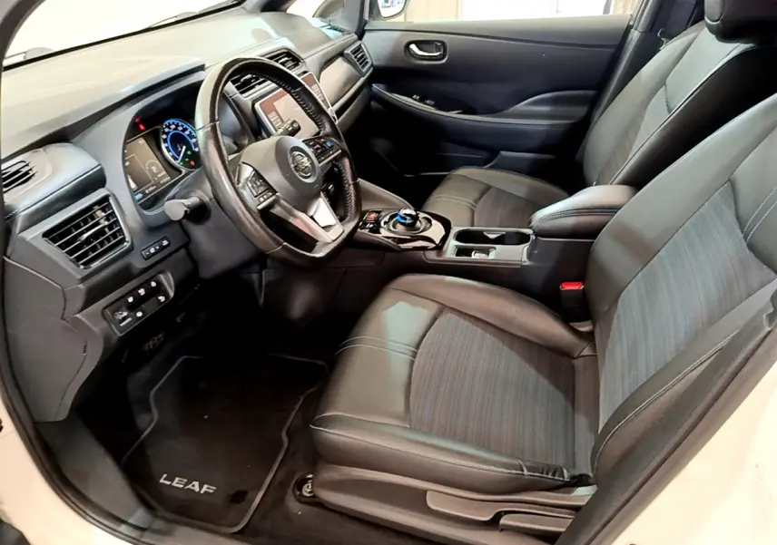 Vue intérieure côté conducteur du Nissan Leaf blanc 2020, montrant sièges cuir et tableau de bord avec écran tactile.