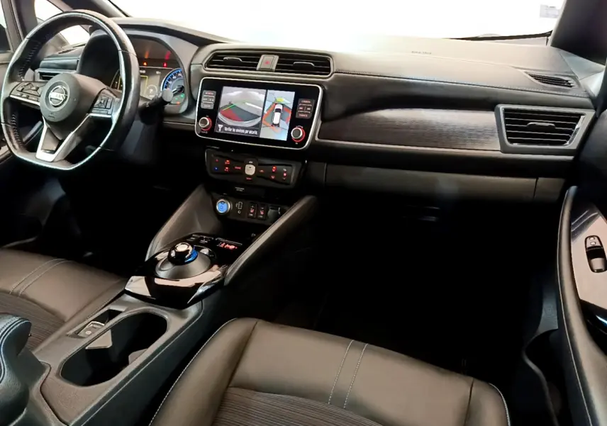 Vue intérieure avant du tableau de bord et volant cuir noir du Nissan Leaf blanc avec écran tactile et commandes au volant.
