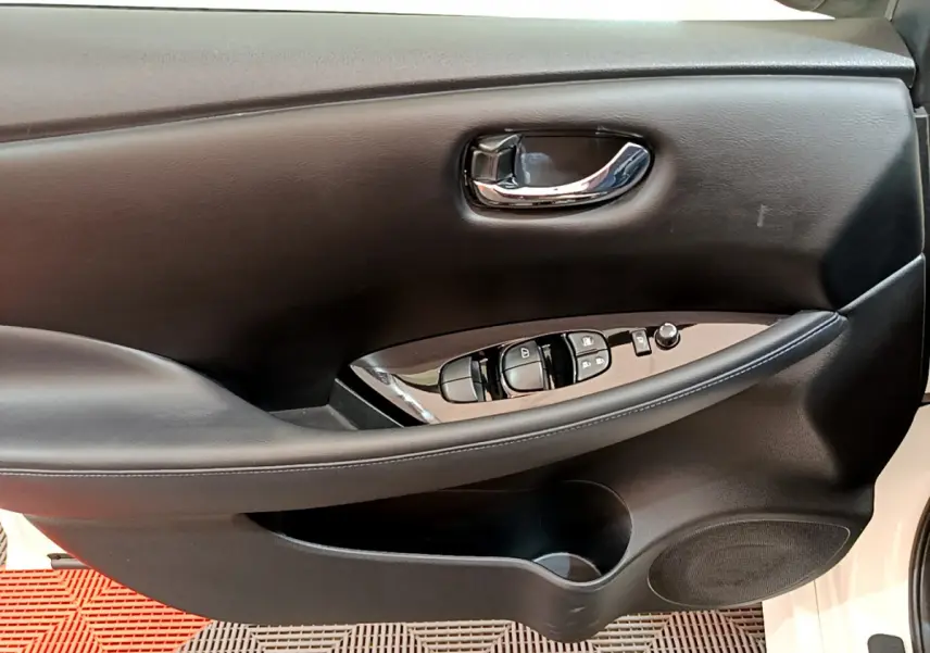Intérieur côté conducteur de la porte noire d'une Nissan Leaf blanche, avec commandes électriques et poignée chromée.