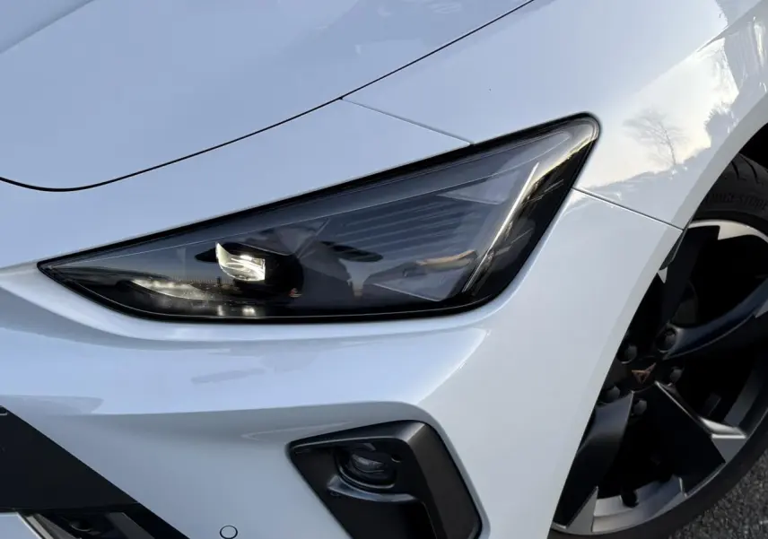 Gros plan sur l'avant droit blanc neige de la CUPRA Leon 2025, mettant en valeur le phare Tri-LED et la jante alliage 18 pouces.