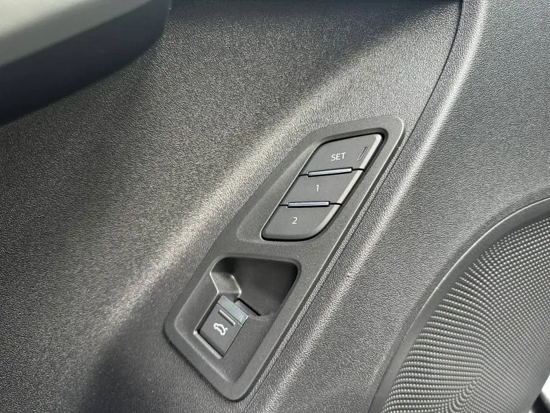 Détail des boutons de réglage mémoire des sièges et ouverture du coffre sur la porte intérieure d’un Audi Q3 gris 2026.