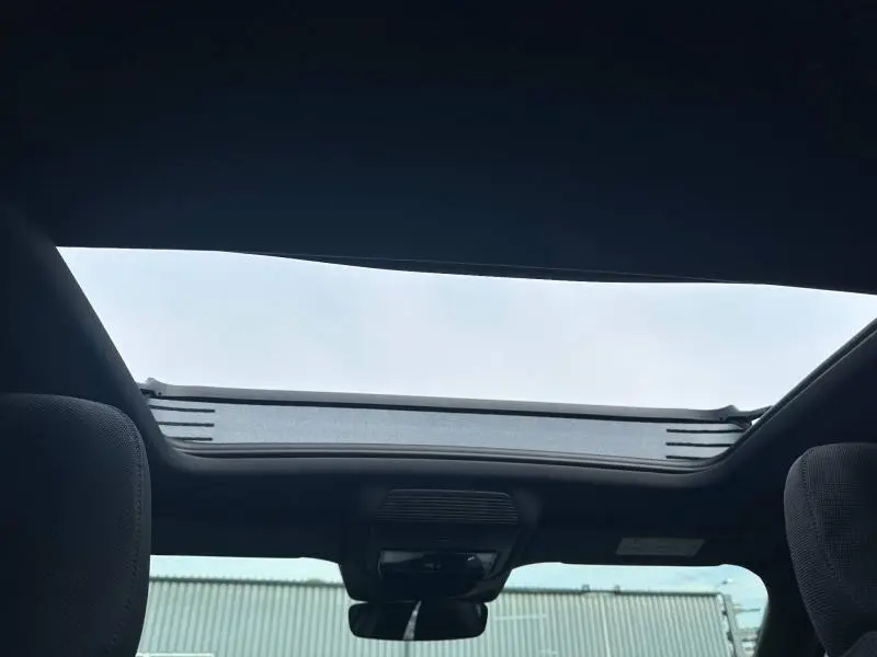 Toit ouvrant panoramique ouvert vu de l'intérieur d'un Audi Q3 gris 2026, avec ciel visible au-dessus.