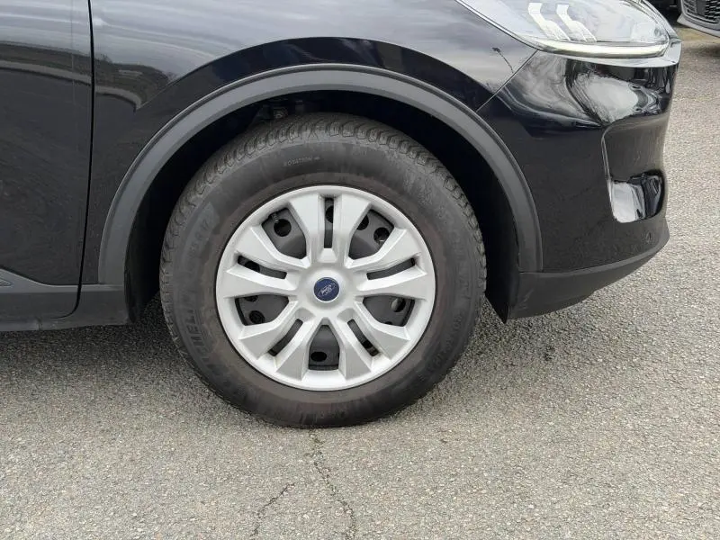 Gros plan sur la roue avant gauche du Ford Kuga 2024 noir, avec jante argentée et logo Ford au centre.
