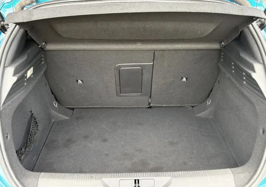 Coffre ouvert vu de l'arrière d'une Peugeot 308 2024 Bleu Obsession avec intérieur noir et filet de rangement latéral.