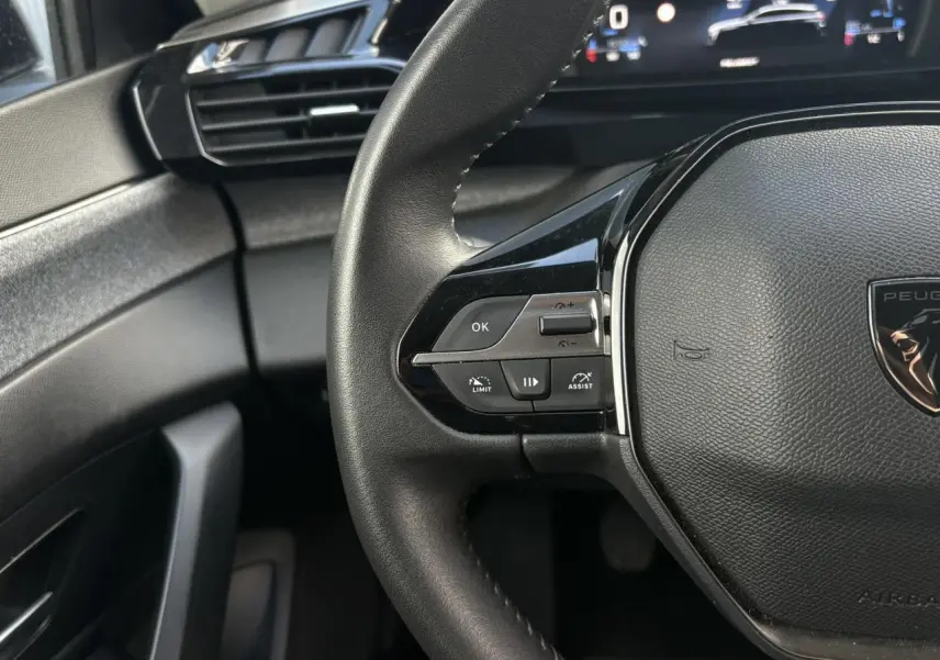 Gros plan sur le volant cuir noir de la Peugeot 308 2024 avec commandes intégrées et tableau de bord numérique.