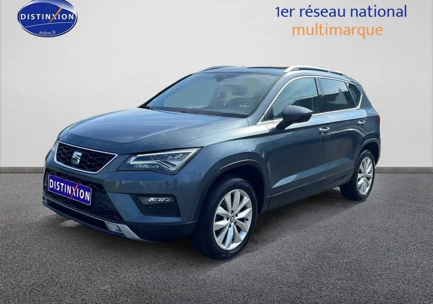 SEAT Ateca bleu/gris en 3/4 avant droit, avec jantes alu et barres de toit visibles.