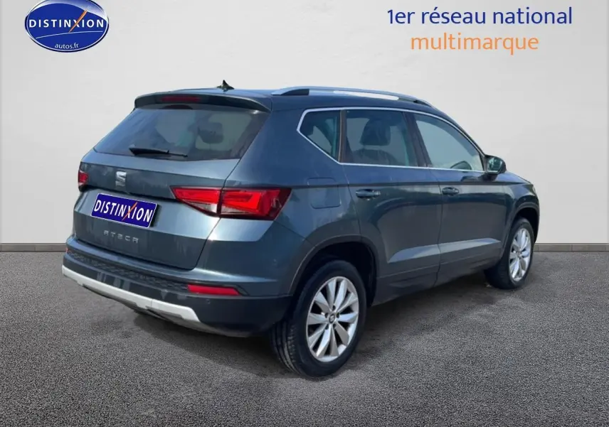 Vue 3/4 arrière droite d'un SEAT Ateca bleu/gris avec jantes alu et barres de toit visibles.