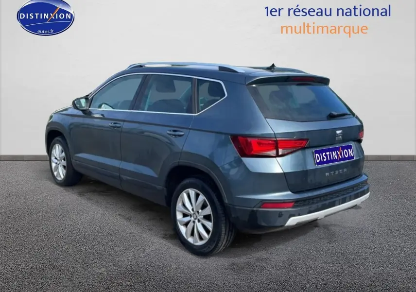 Vue 3/4 arrière droite d'un SEAT Ateca bleu/gris avec jantes alu et barres de toit visibles sur fond neutre.