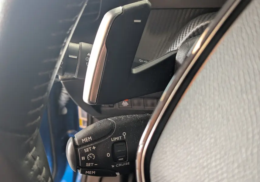 Gros plan sur la commande de régulateur de vitesse et palettes au volant dans l’habitacle d’un Peugeot 2008 bleu.