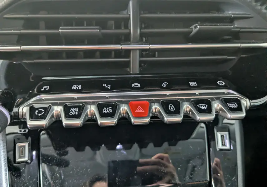 Gros plan sur la rangée de boutons chromés et noirs du tableau de bord du Peugeot 2008, avec bouton rouge d'alerte.