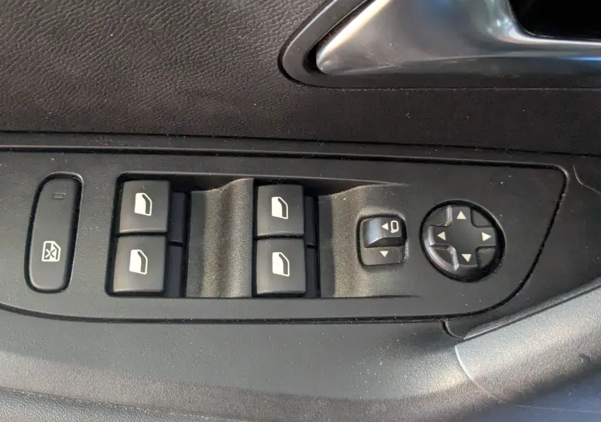 Gros plan sur les commandes de lève-vitres et réglage des rétroviseurs côté conducteur d'une Peugeot 2008 bleu.