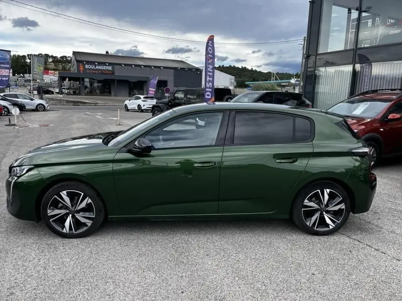 Vue de profil côté gauche d'une Peugeot 308 1.2 PureTech 130 Allure 2023 en vert olivine, avec jantes alliage distinctives.