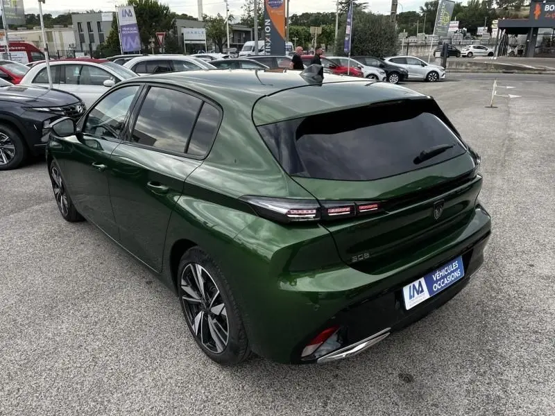 Vue 3/4 arrière droite d'une Peugeot 308 1.2 PureTech 130 Allure 2023 en vert olivine avec vitres teintées et jantes alliage.