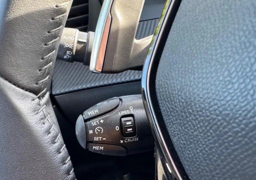 Gros plan sur la commande de régulateur de vitesse au volant cuir noir du Peugeot 2008 Hybrid 136 e-DCS6 Allure.