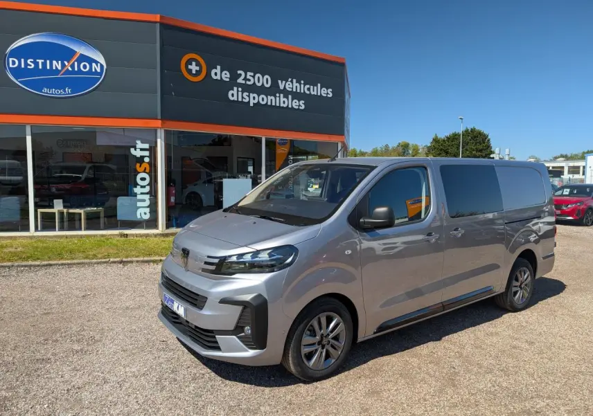 Vue 3/4 avant droit d’un Peugeot Expert Fourgon gris métallisé avec jantes alliage et vitres teintées, stationné devant un concessionnaire.