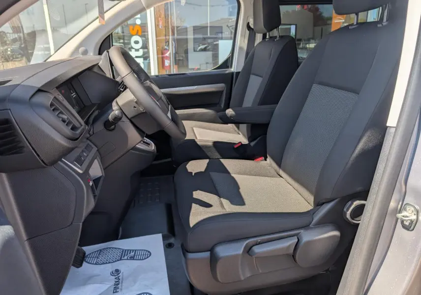 Vue intérieure côté conducteur du Peugeot Expert Fourgon XL 2026, sièges tissu bi-ton gris et noir avec accoudoirs.